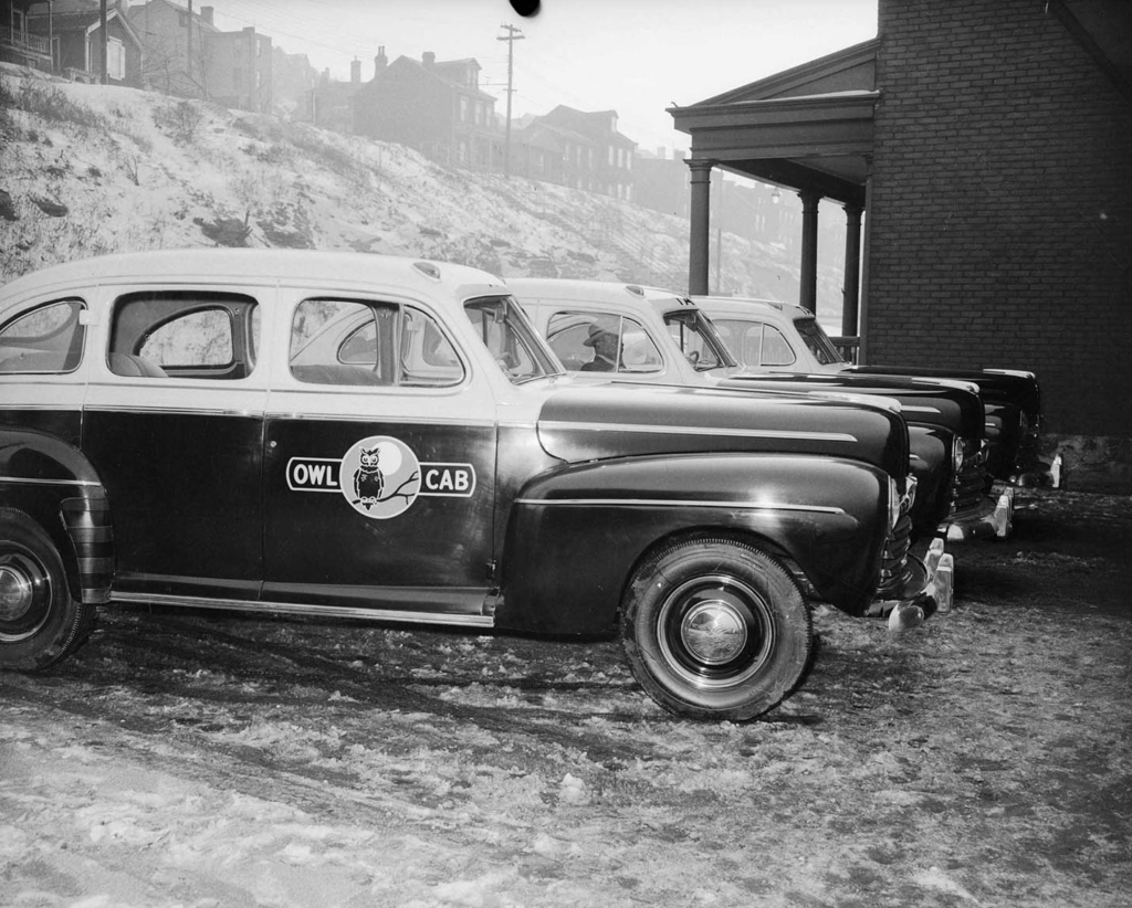 Photograph by Charles Teenie Harris of Owl Cab Taxis side-by-side in a parking lot.