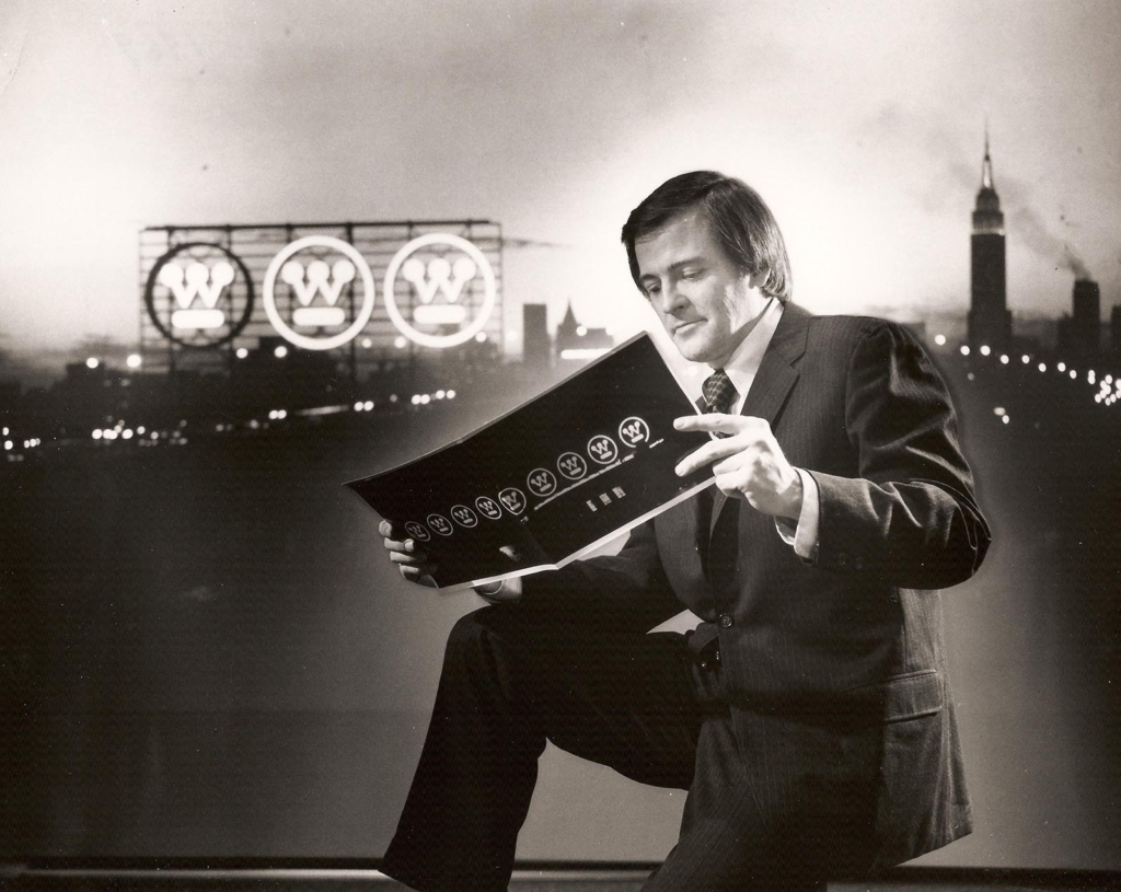 Black and white photograph of a man in a suit looking at a flyer with Westinghouse logos on it.