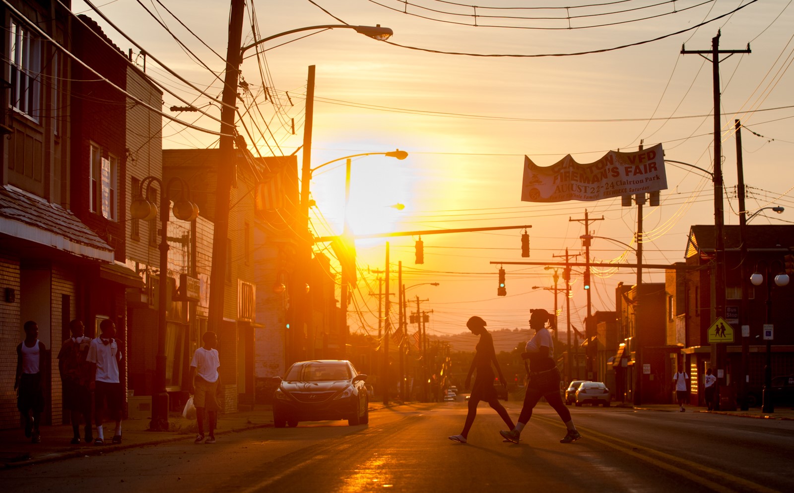 The sun sets on two silhouettes crossing a road.