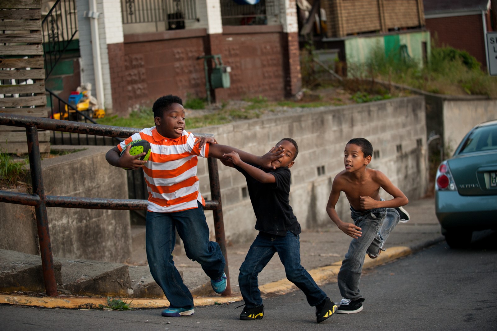 Three kids play football in the street.