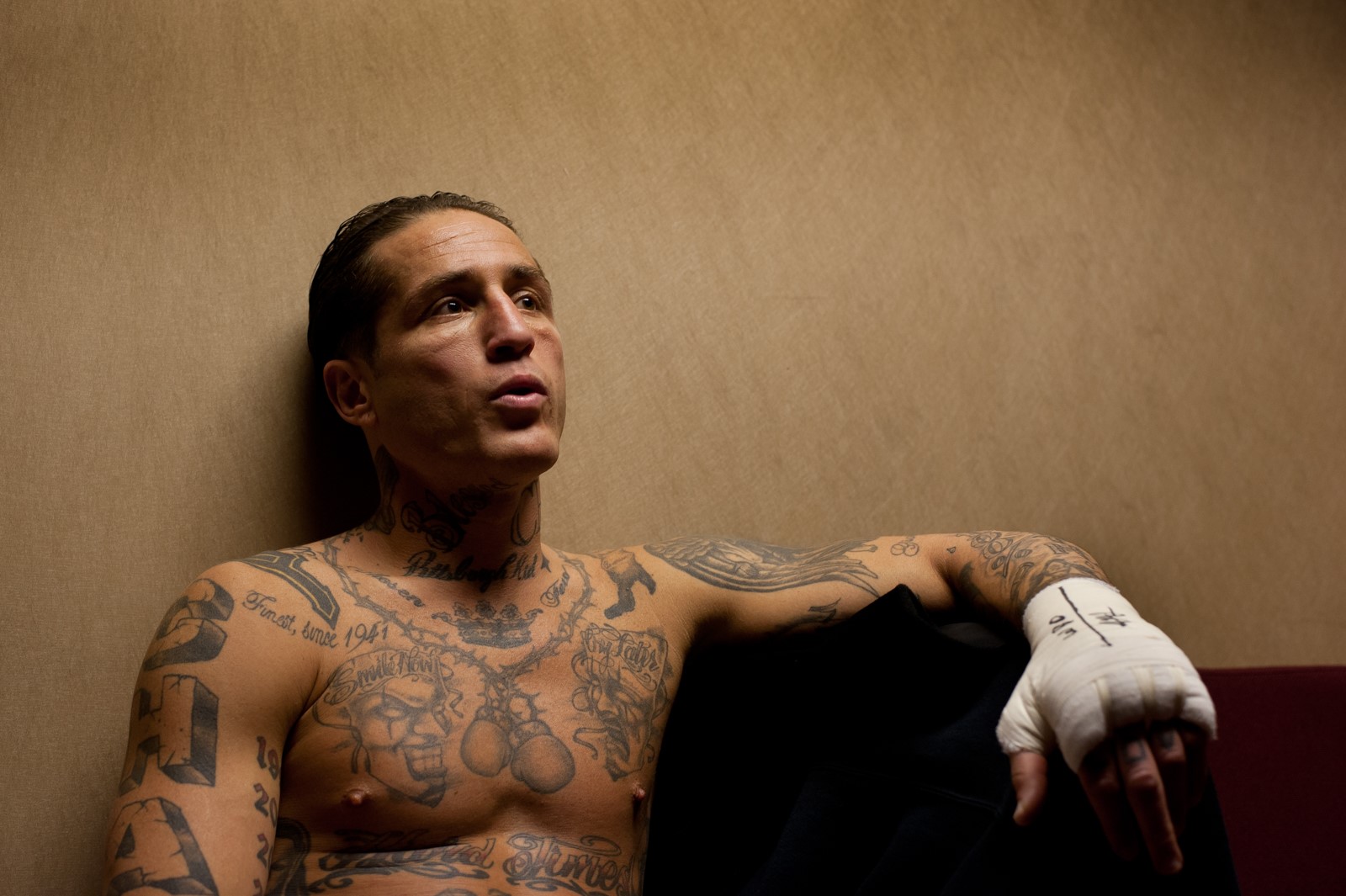 A tattooed boxer sits on a couch, looking into the distance.