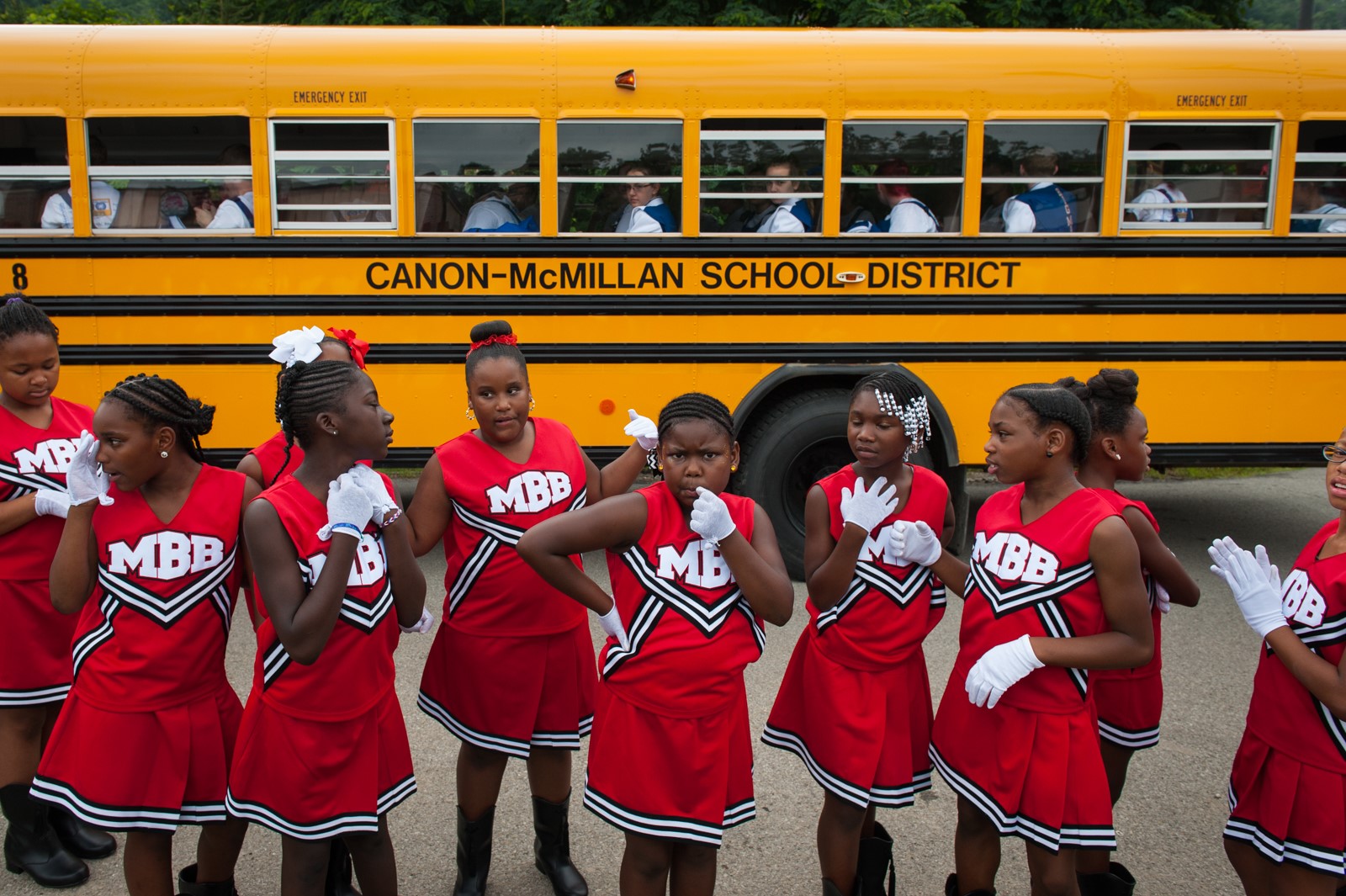 Young cheerleaders pose in front of a school bus.