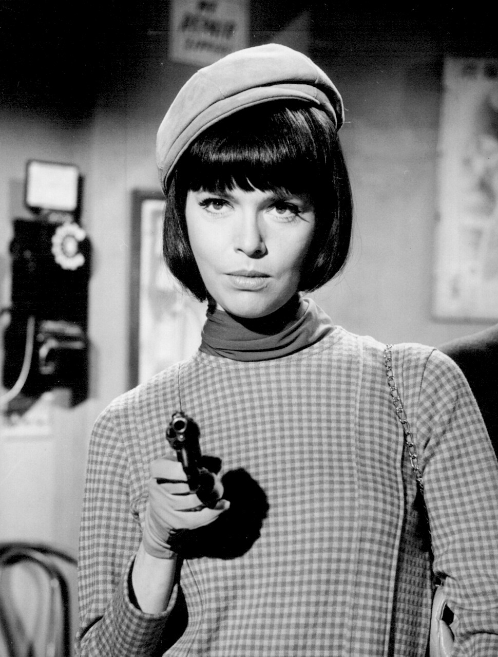 Still from a TV show depicting a well-dressed woman aiming a handgun.