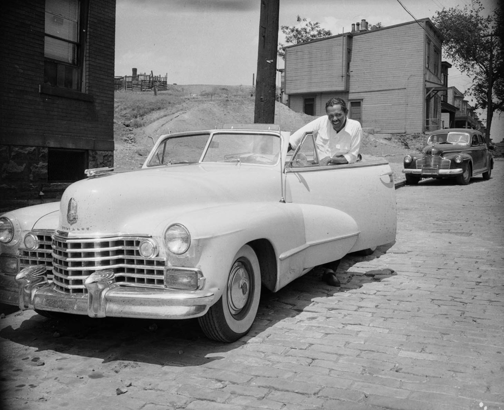 Black and white photograph of a man in a Cadillac convertable.