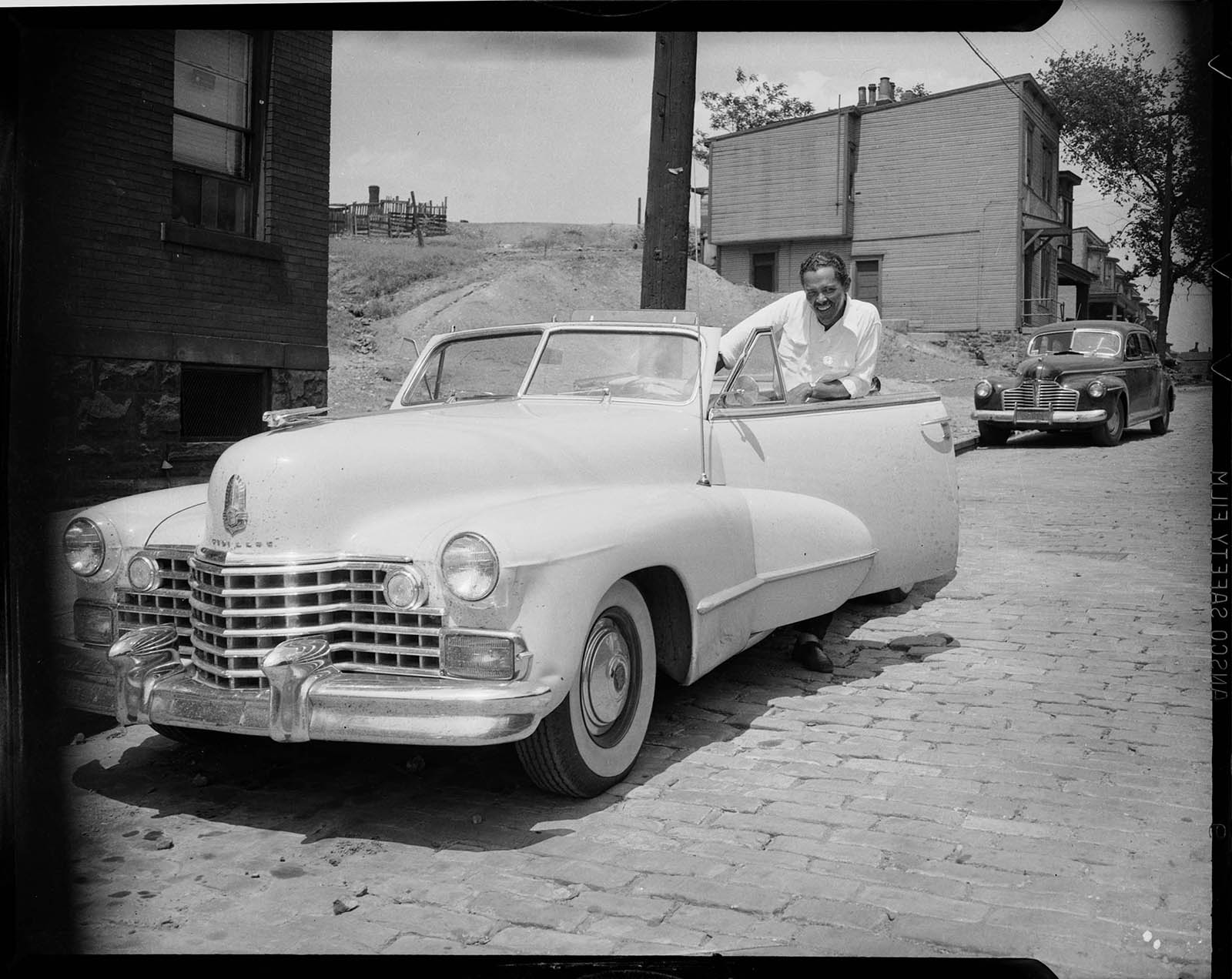 Black and white photograph of a man in a Cadillac convertable.