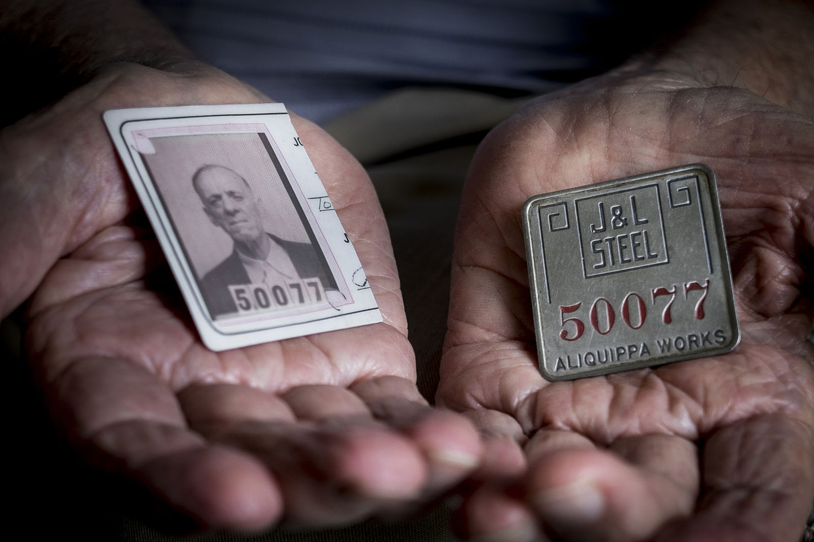 Hands holding a steel company badge and a cut-in-half ID.
