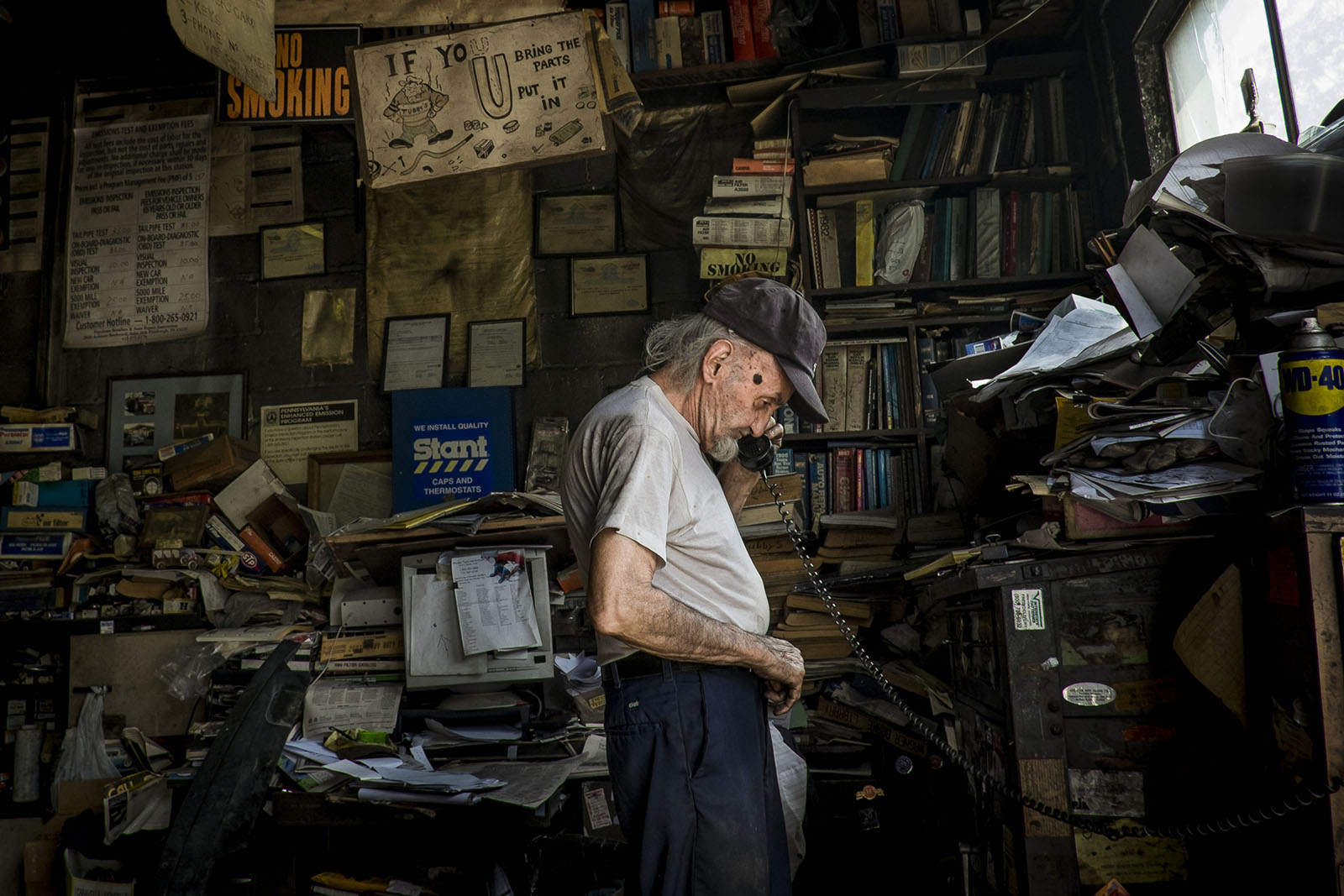 A man talks on the landline telephone at his dingy repair shop.