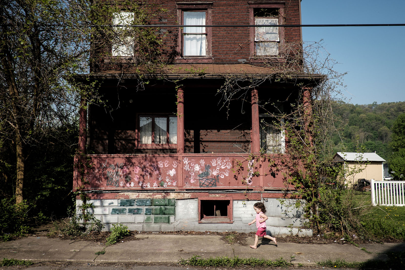 A young girl runs by a decrepit, abandoned house.