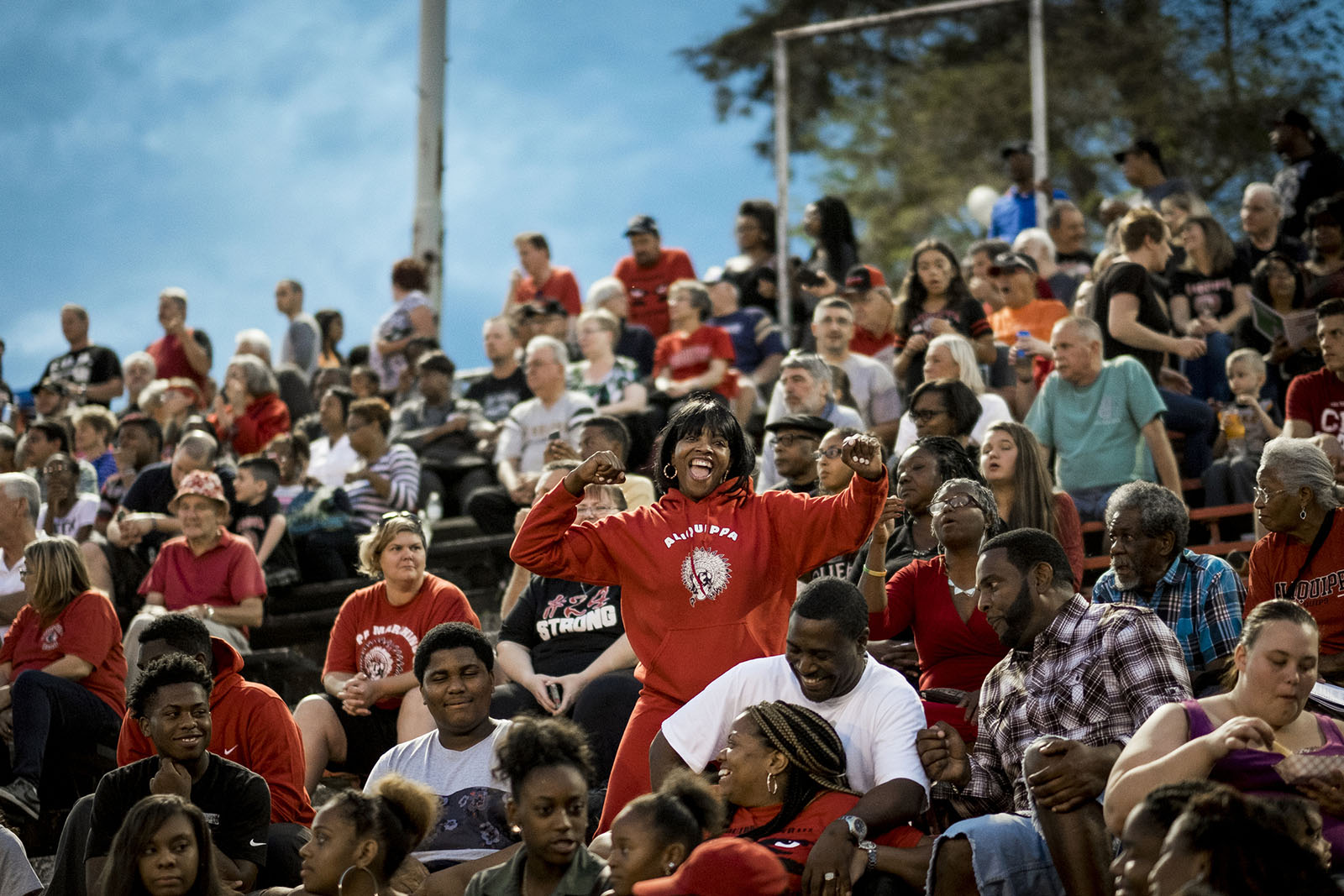 Wide shot of mostly sitting Aliquippa fans at a high school football game.