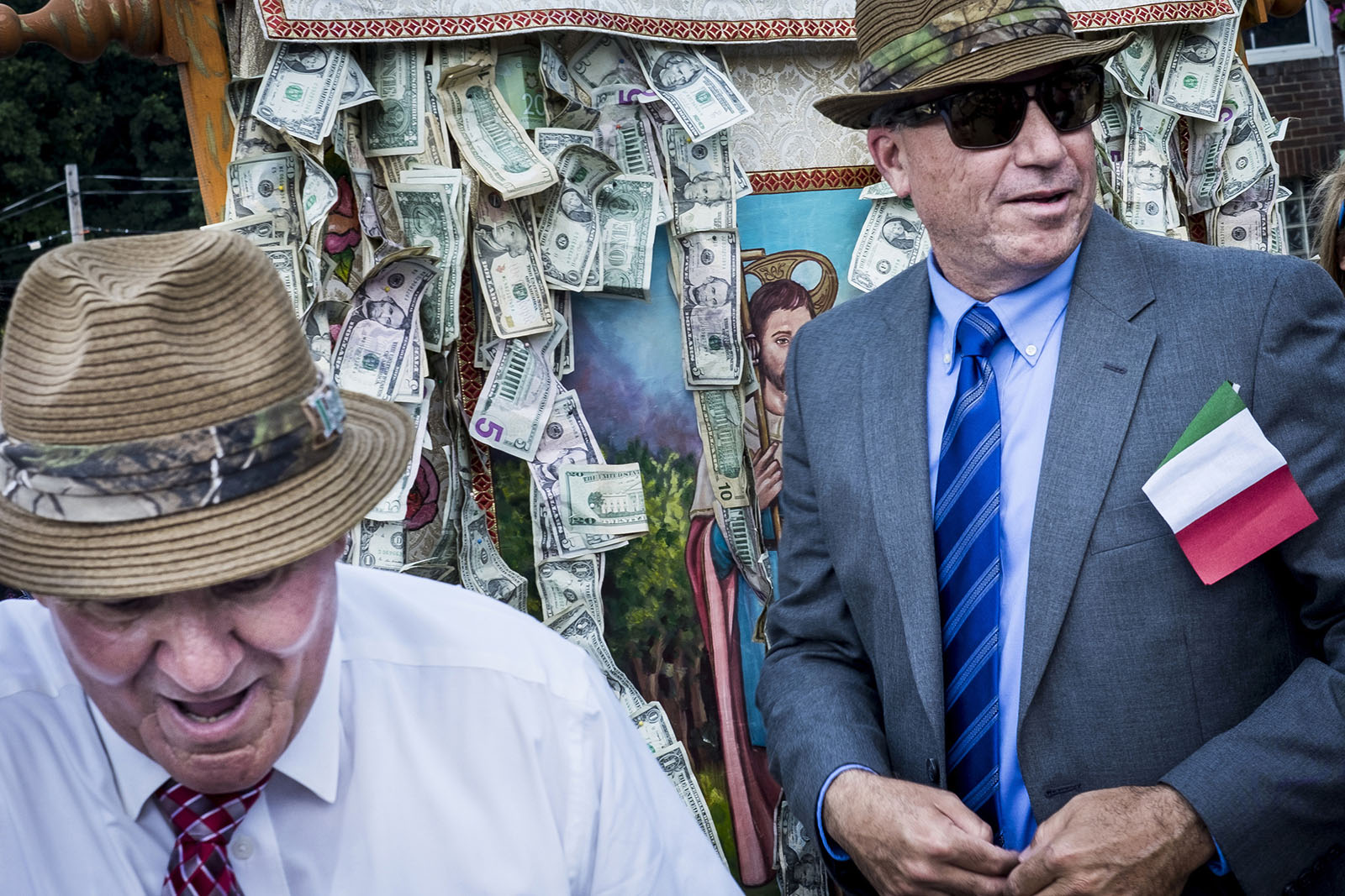 Two men, one with an Italian flag, stand by a wall of multi-valued bills.