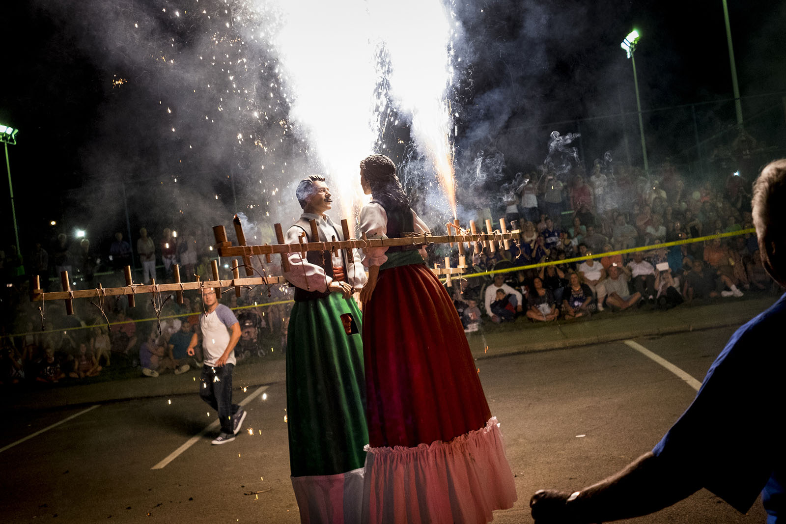 Two dolls dance together while fireworks are lit brightly in the background.