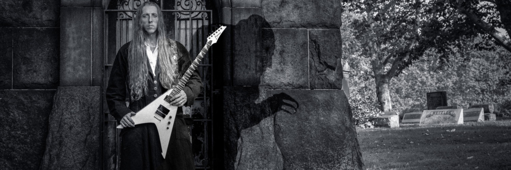 Musician George Sabol stands with a guitar in a cemetery with the shadow of Nosferatu looming
