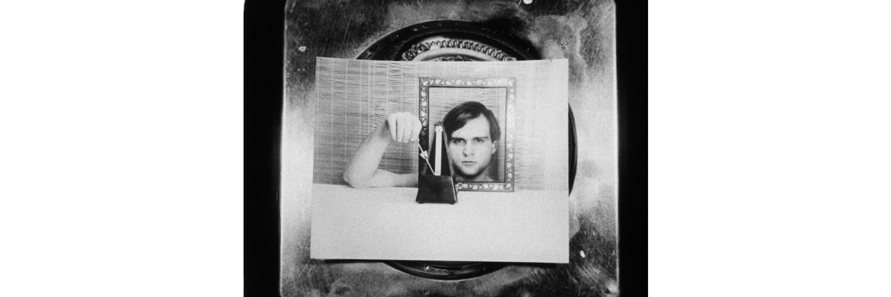 Film still showing photograph of a man's face and arm. The photograph sits on a stove burner