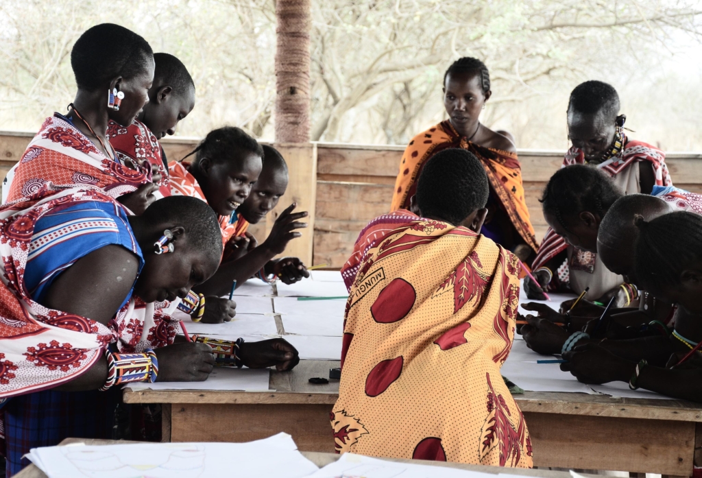 Women artisans in Kenya gathered around a table sketching and talking