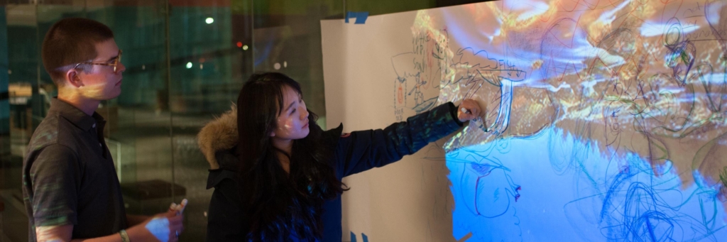 Two people trace shapes projected onto a large sheet of paper