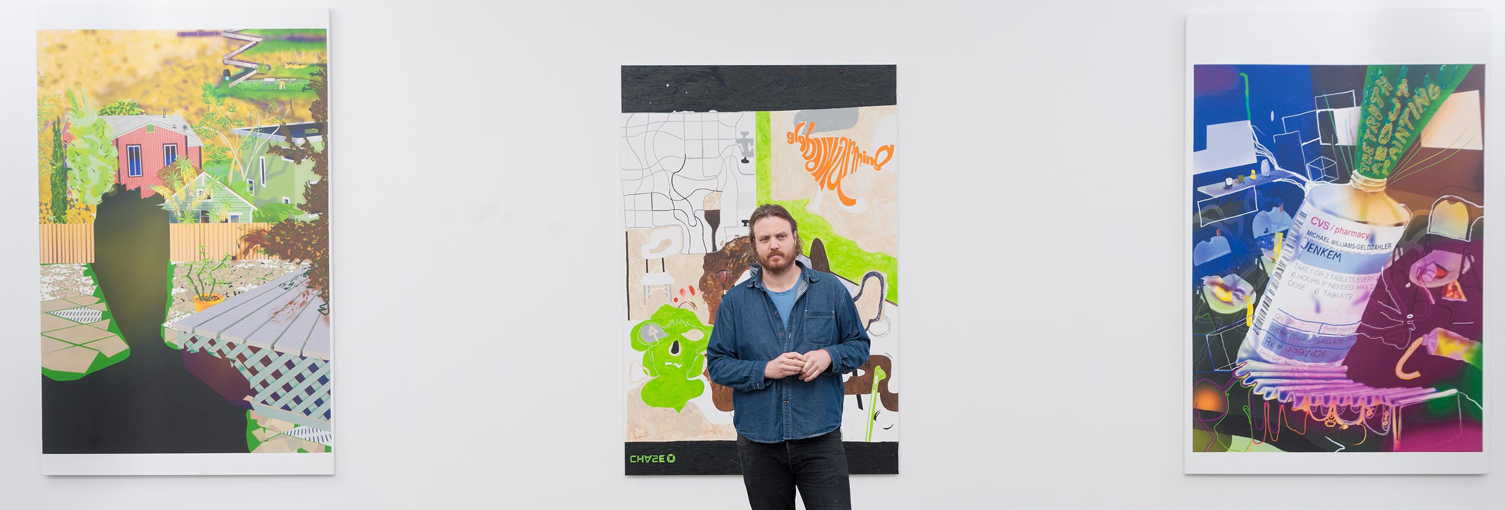 Artist Michael Williams stands in a gallery with 3 large colorful canvases behind him.