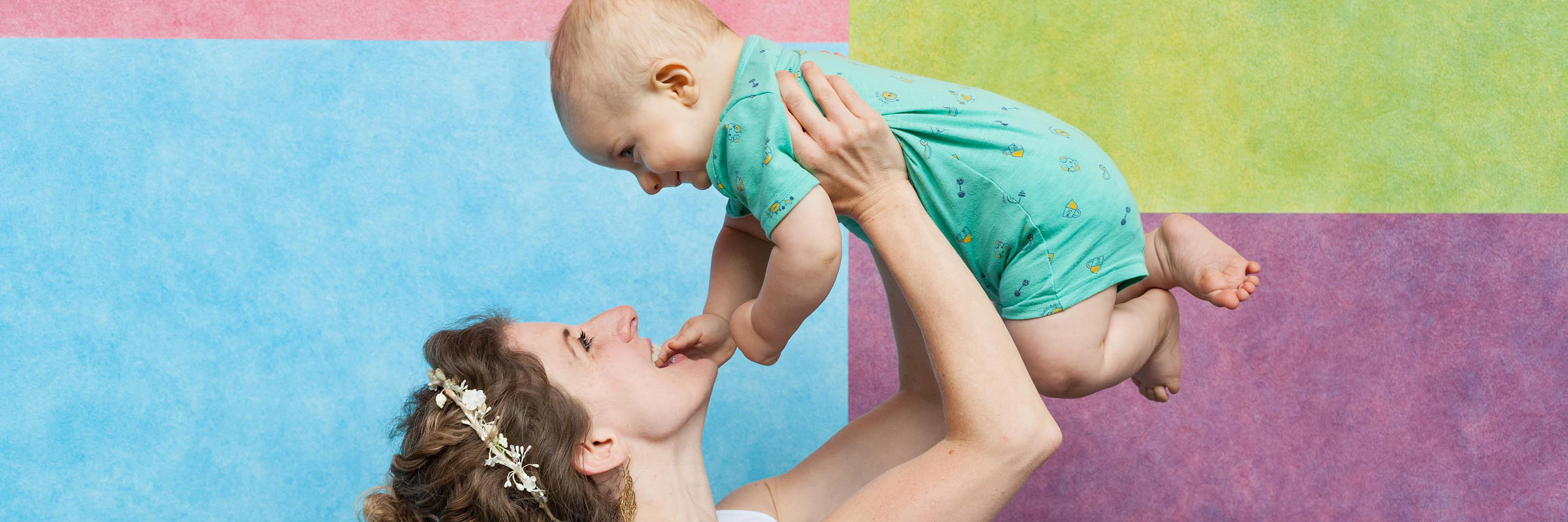 A woman holds a baby aloft in front of a painted wall.