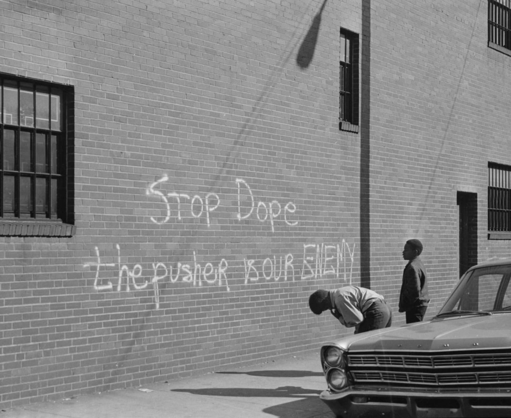Photography by Charles Teenie Harris of a chalk on brick wall that says Stop dope the pusher is our enemy