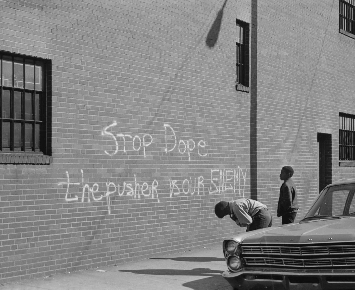 Photography by Charles Teenie Harris of a chalk on brick wall that says Stop dope the pusher is our enemy