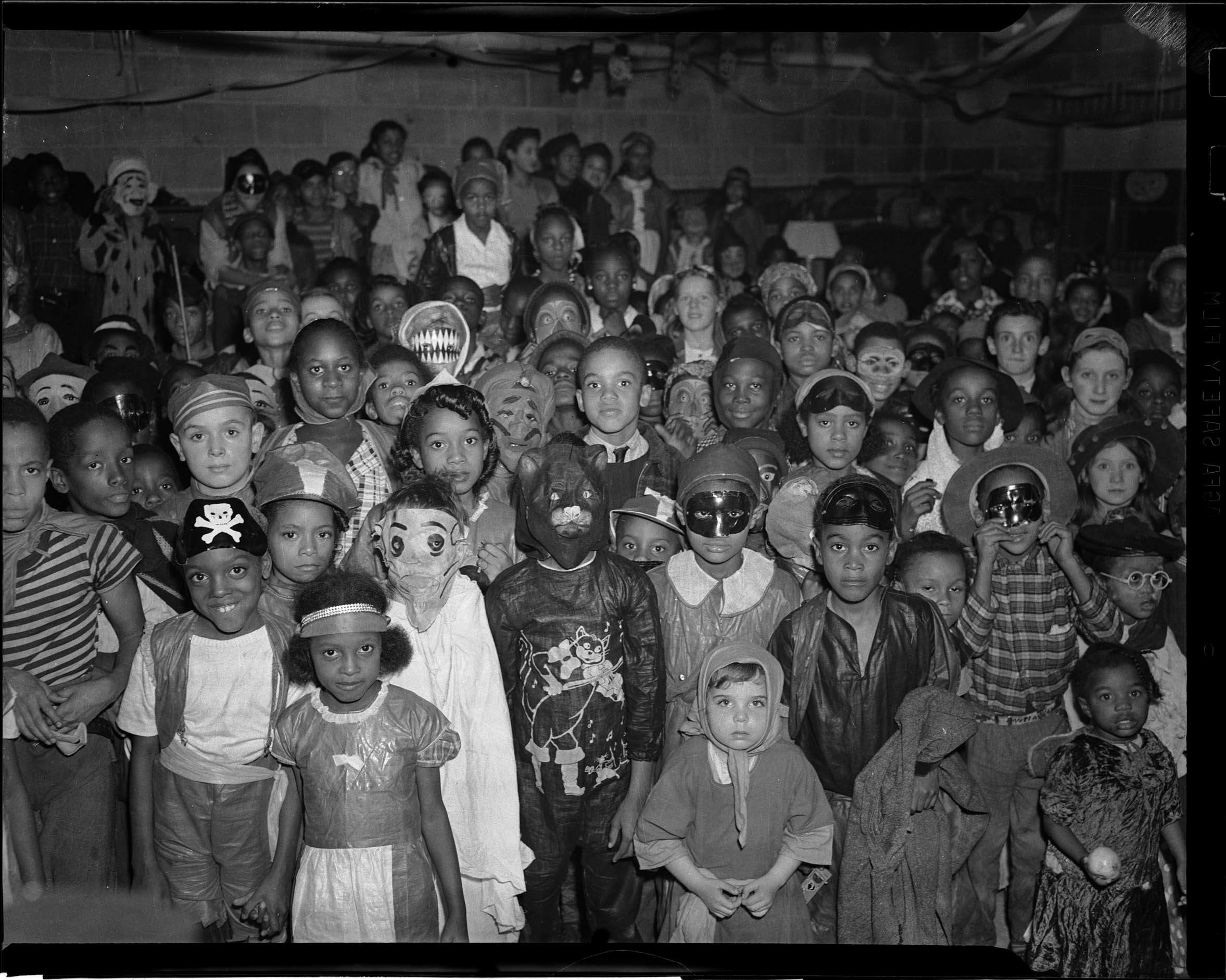 Crowd of children, all facing the camera, wearing costumes, including pirates, masked heroes, and monsters