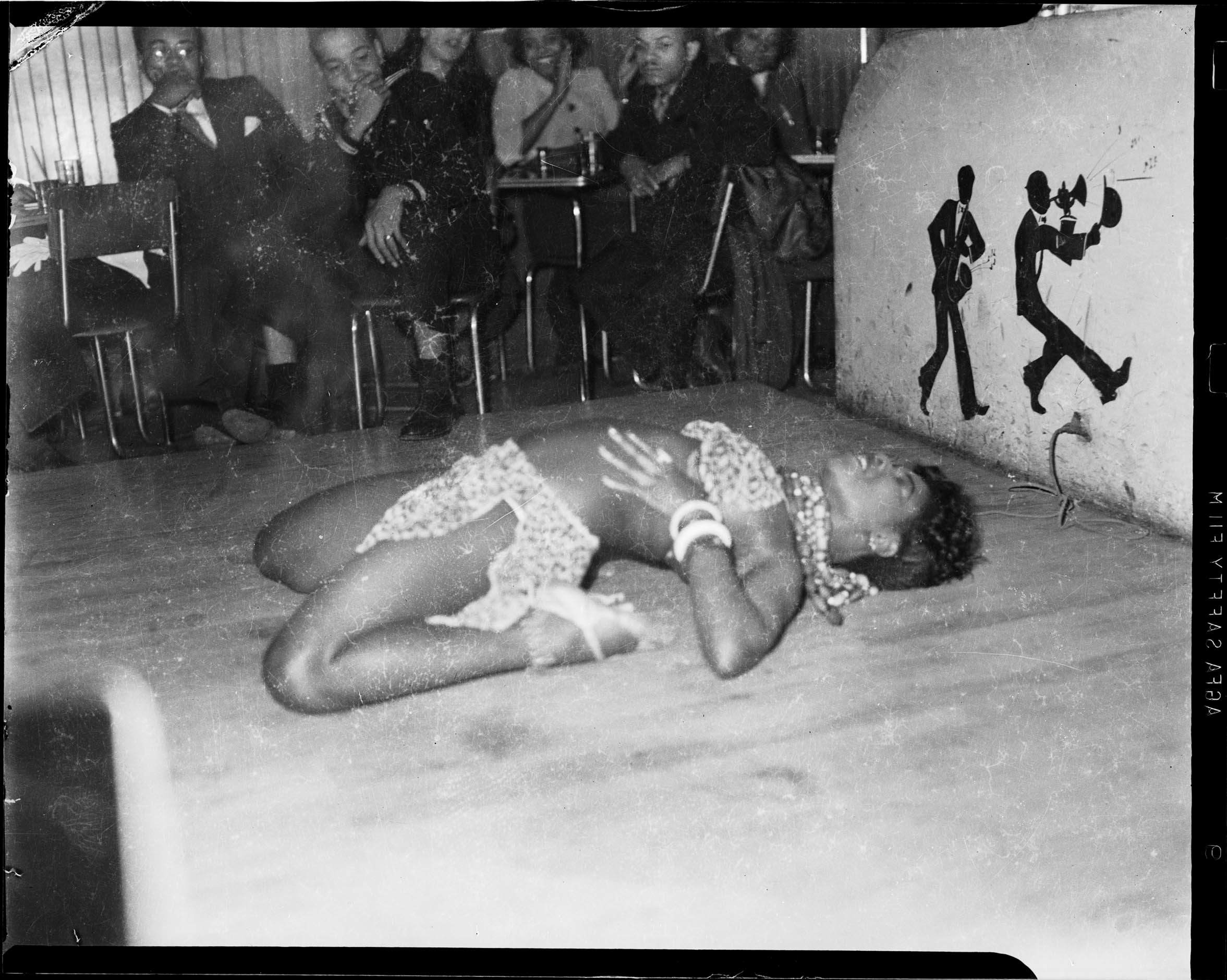 Female dancer in two piece costume bending over backwards on stage with jazz musician caricatures decoration