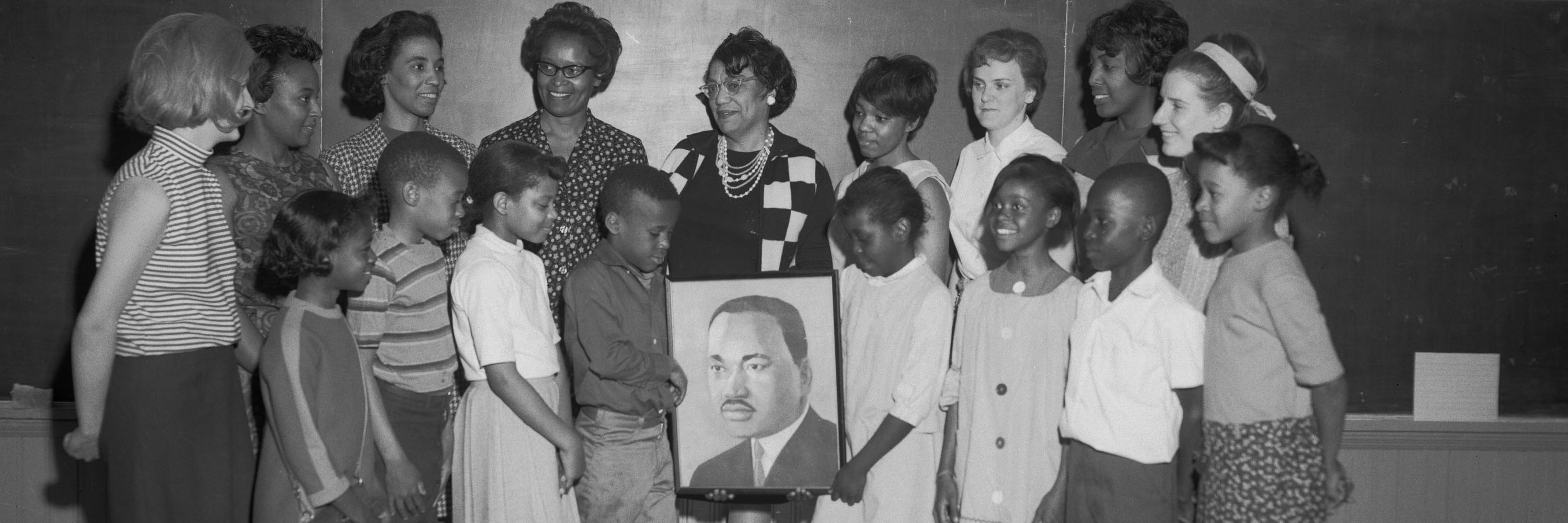 An image of a group gathered around a photo of Martin Luther King Jr., with two children in the front of the group holding up the framed photo.