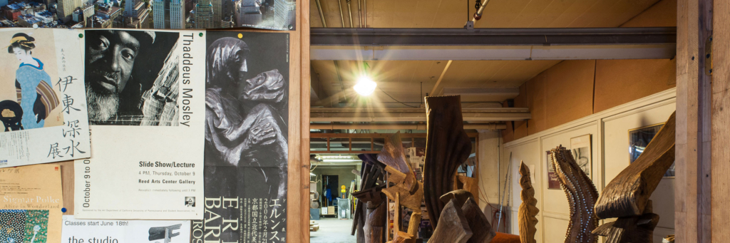 Open doorway with a view of a large workspace dotted with wooden sculptures.