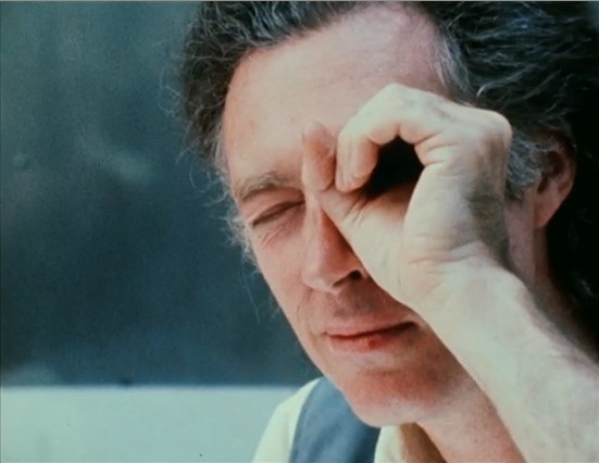 A man squints from a photo. His left hand, held up to his left eye, forms a circle that resembles a scope or director's viewfinder.