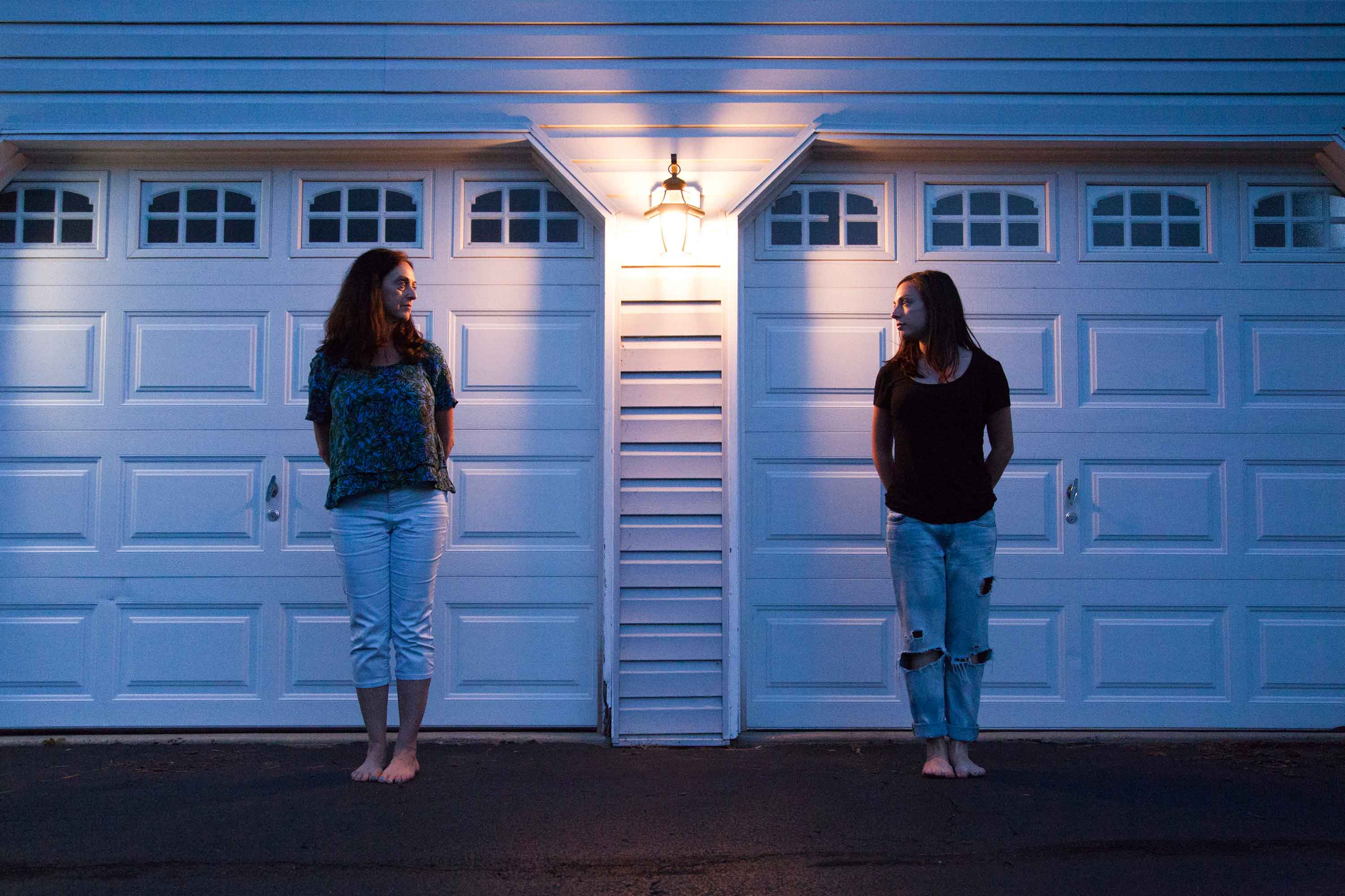 Mother and daughter standing in a driveway at night staring at one another.