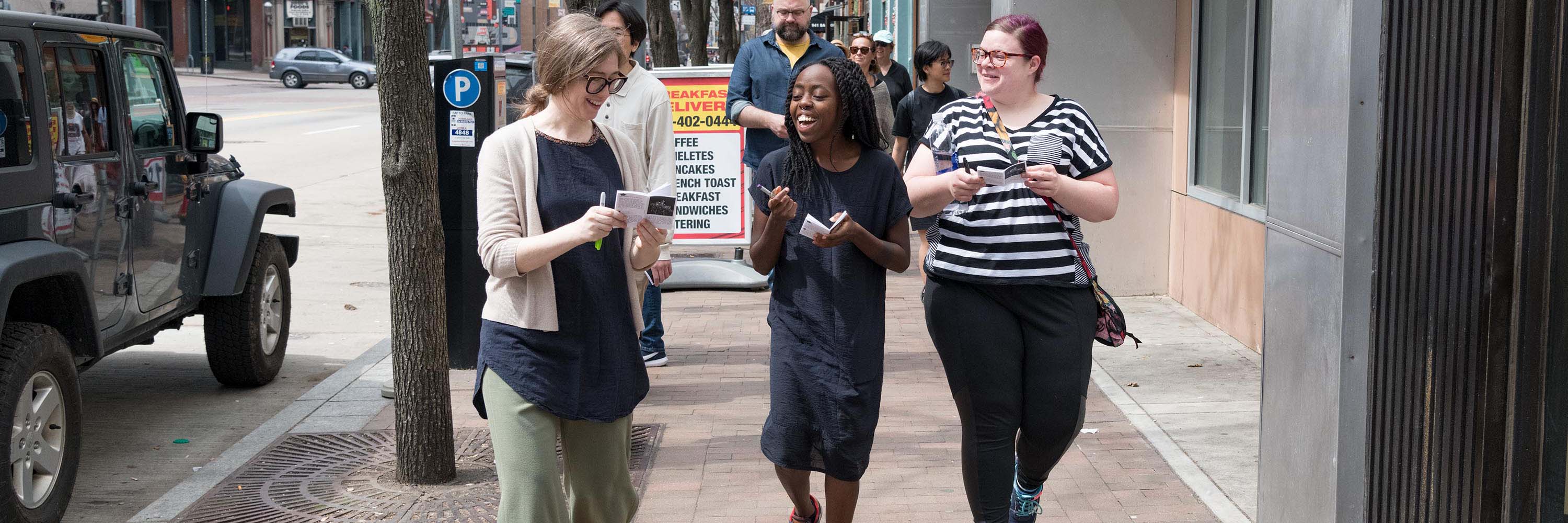 Three women walking down a sidewalk sketching