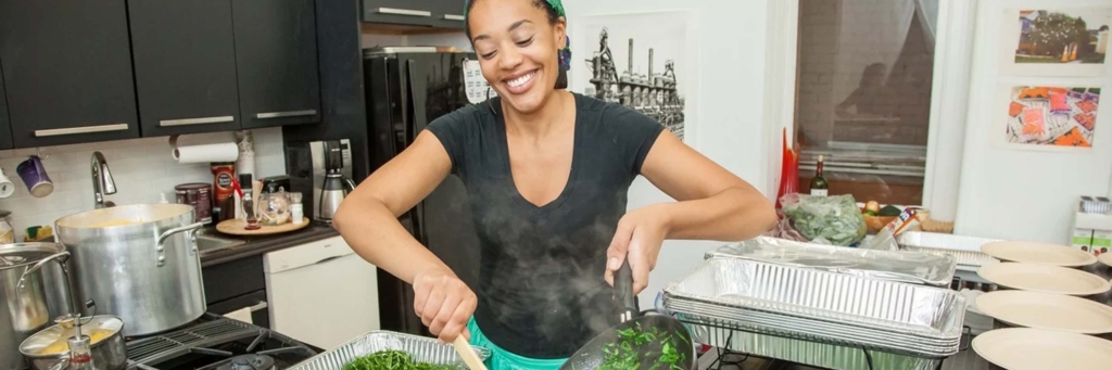 Chef Keyla Nogueira Cook scraping greens out of a frying pan