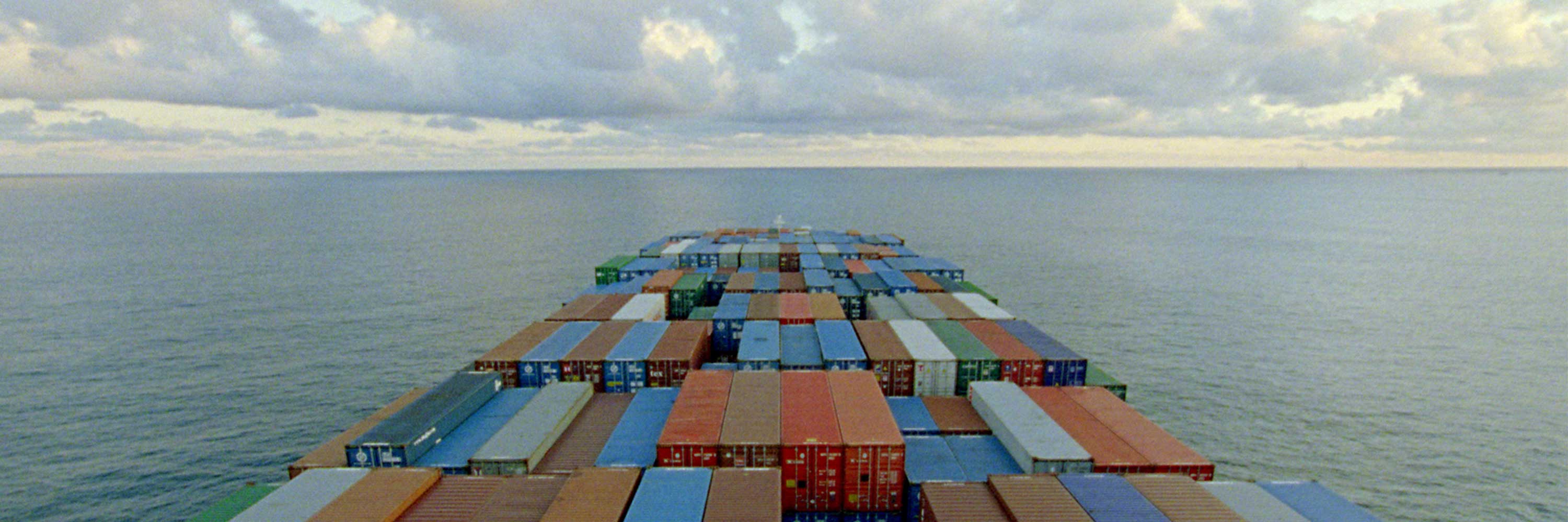 A group of different colored shipping containers near water under a cloudy sky.