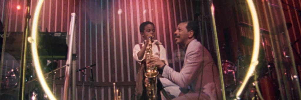 Ornette Coleman on stage while young boy plays the saxophone.