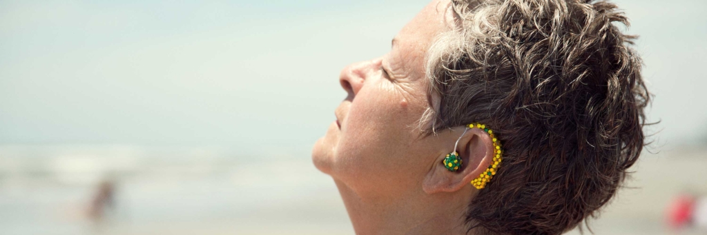 A woman leans her head back, showing a brightly colored jewelry-like hearing aid.