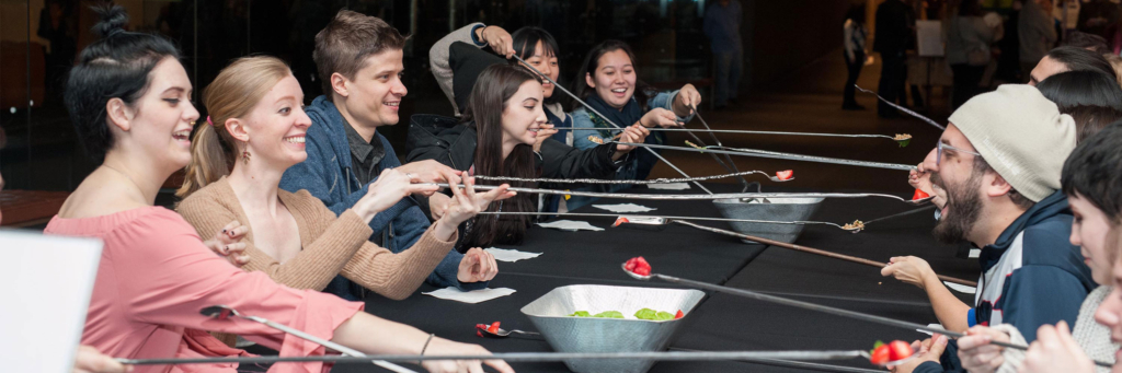 A group of people enjoy the long spoons table, a game where participants try to feed each other across the table using long spoons.