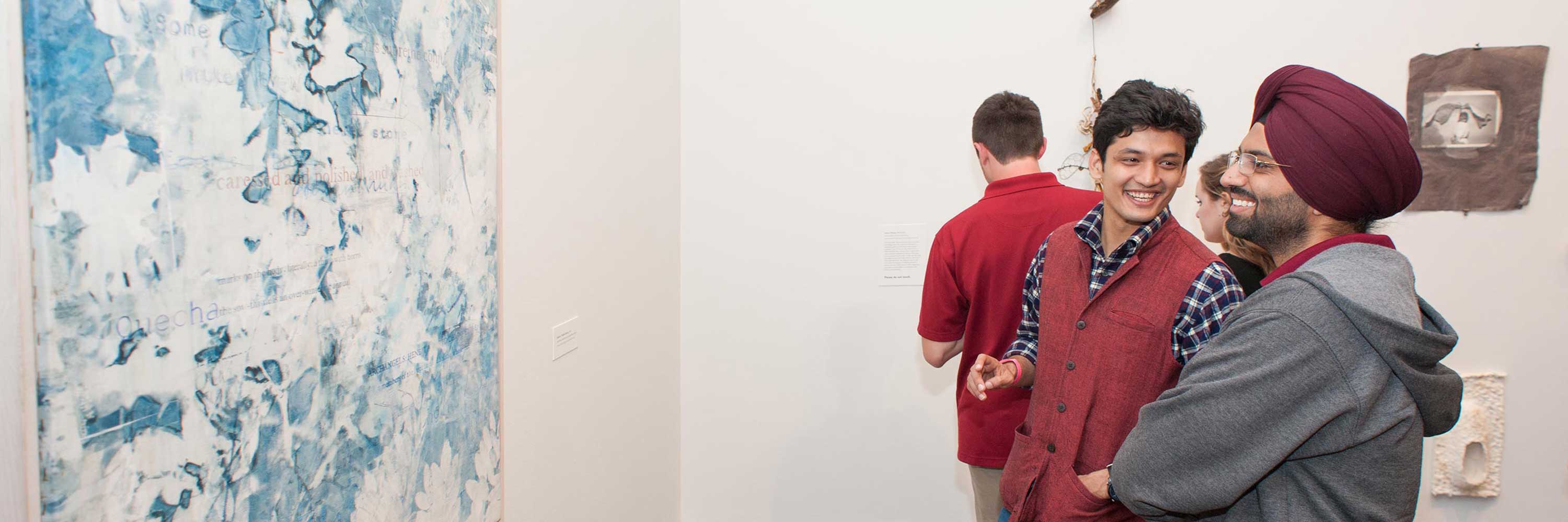 Young men stand in a gallery, smiling at each other
