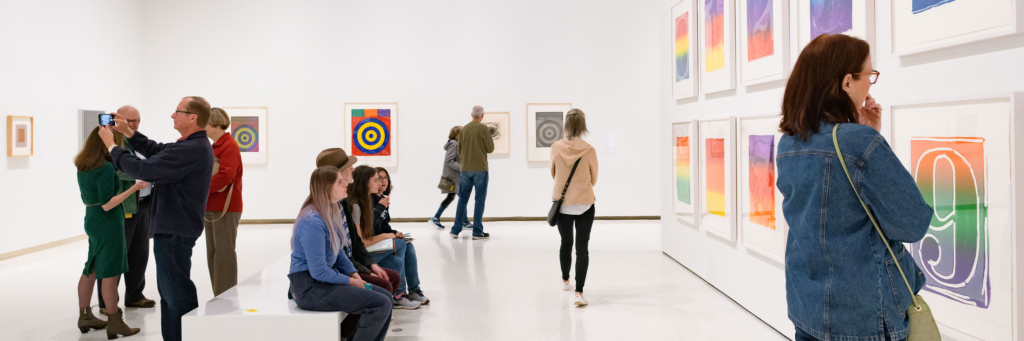 A group of people look at different colorful works in a gallery