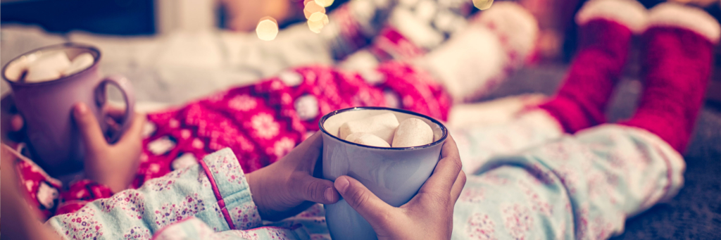 Kids in pajamas sit together, holding mugs of hot chocolate with marshmallows.
