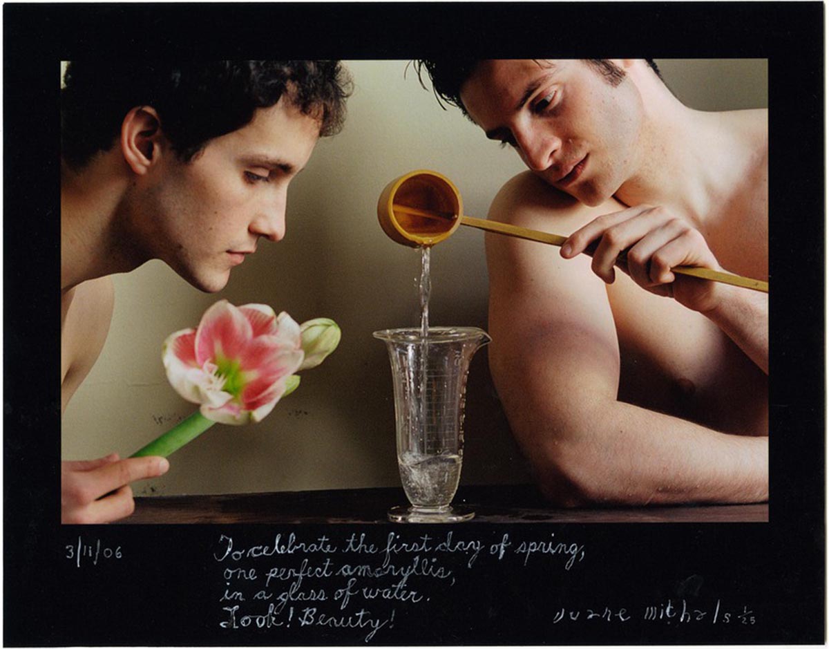 A photograph depicting two shirtless men watching over a glass beaker. Left person holds a flower and the right person pours water into the beaker. Text handwritten on the boarder reads To celebrate the first day of sprint, one perfect amaryllis, in a glass of water. Look! Beauty!