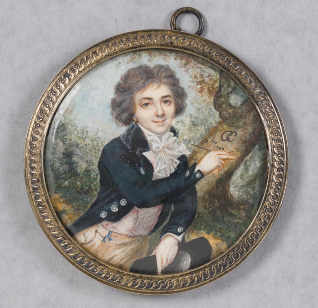 A miniature watercolor portrait of a young man drawing his initials on a tree trunk is painted on a circular piece of ivory with a silver gilt frame.