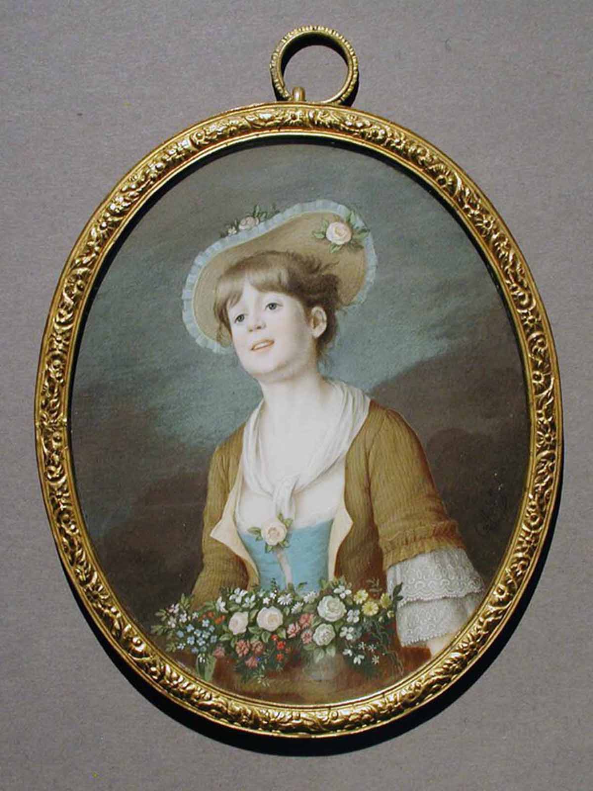 A miniature watercolor portrait of a young woman with a bouquet of flowers at her waist is painted on an oval-shaped piece of ivory with a gold frame.