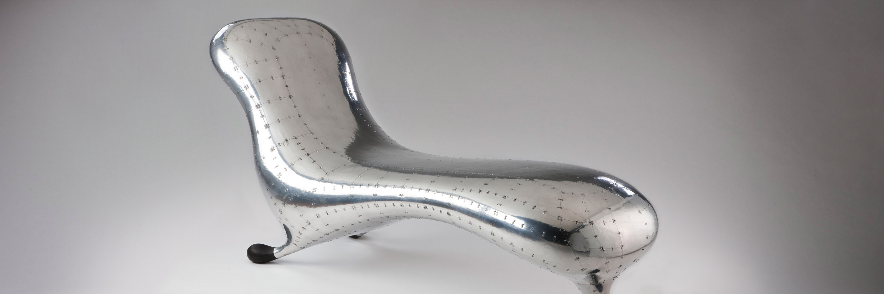 A silver lounge chair with curved, shiny edges and three feet