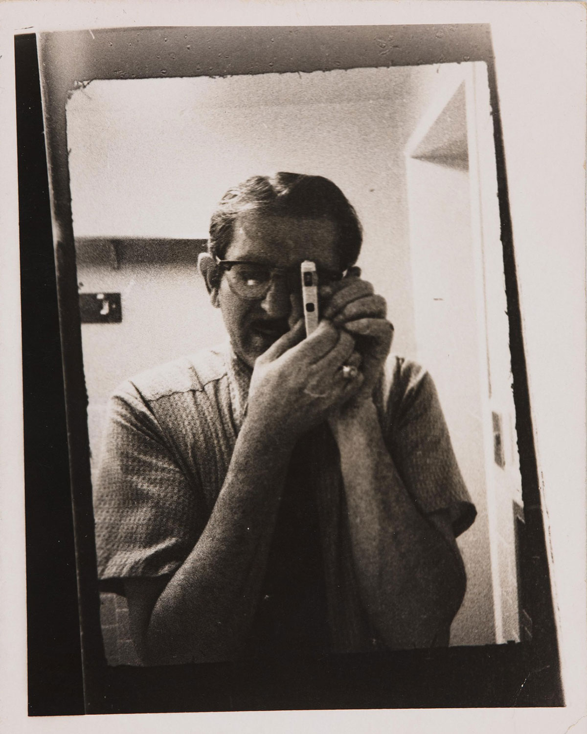 A man wearing a loose t-shirt and glasses holds a small camera up to his eye