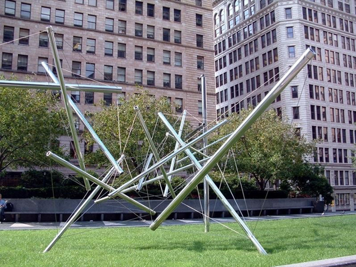 A sculpture made of thin, long metal bars and wires installed on a green space