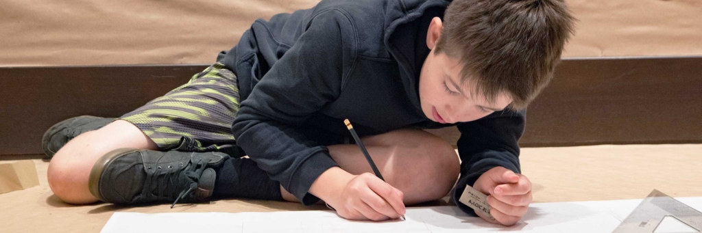 Young person drawing on paper while sitting on the floor with a pencil
