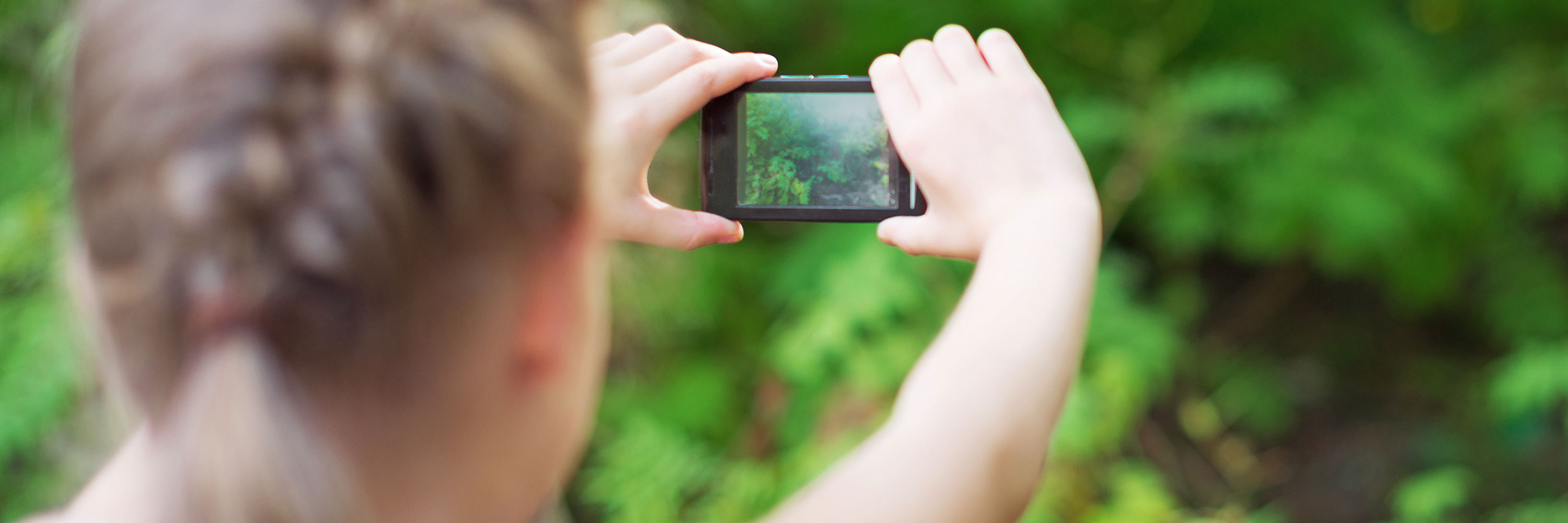 A child facing away from viewer and taking a picture with a smartphone