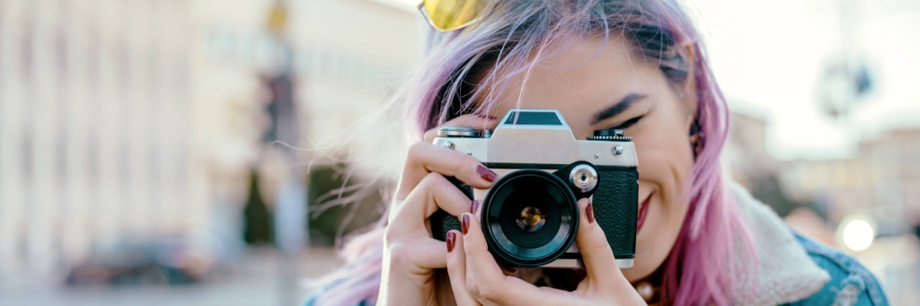 Teen with colorful hair and yellow glasses pointing camera at viewer