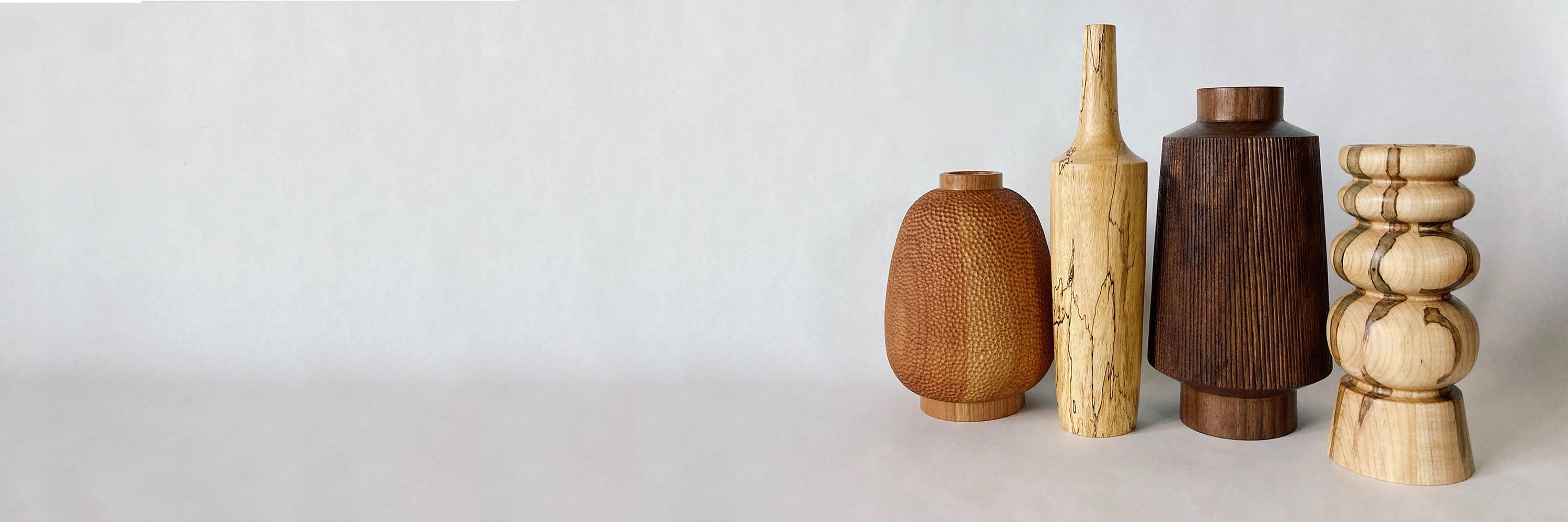 Four wooden vases stand in a cluster; they are each a different shade and shape