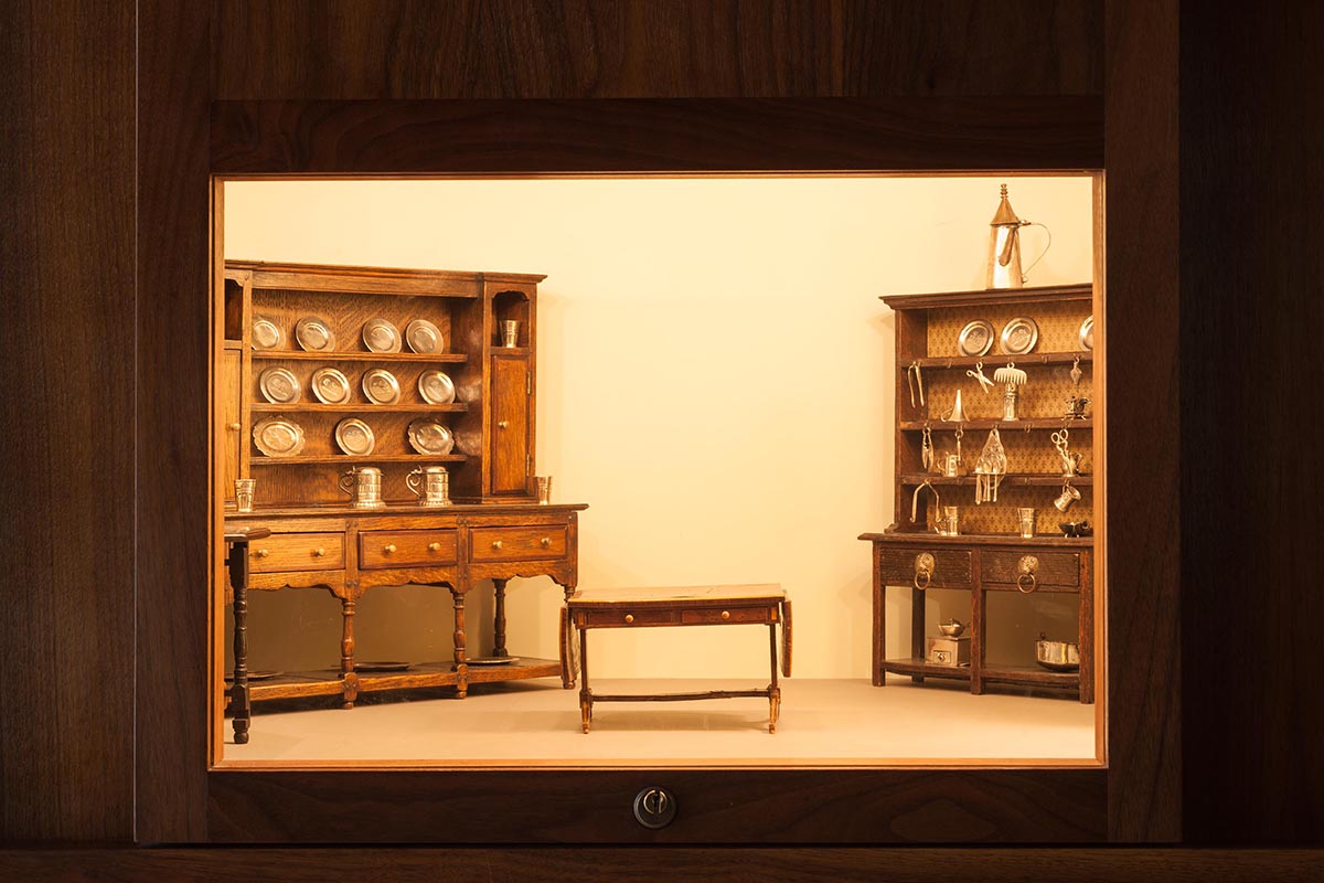 A lit box set inside a wood-paneled wall with miniature models of sideboards filled with dining ware