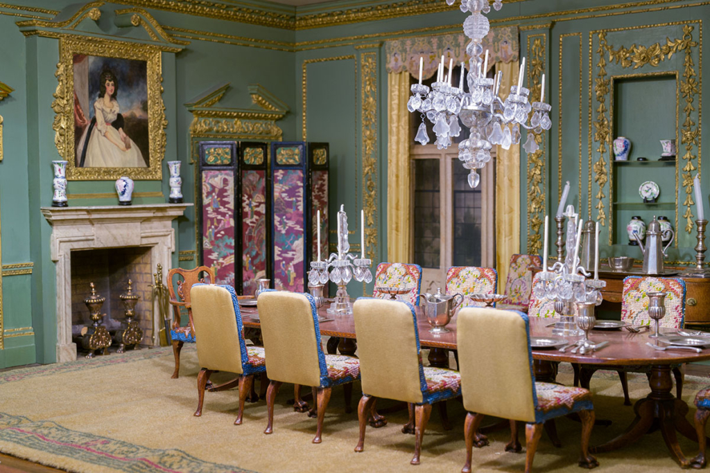 An opulent dining room with a table, fireplace and chandelier crafted out of miniature models